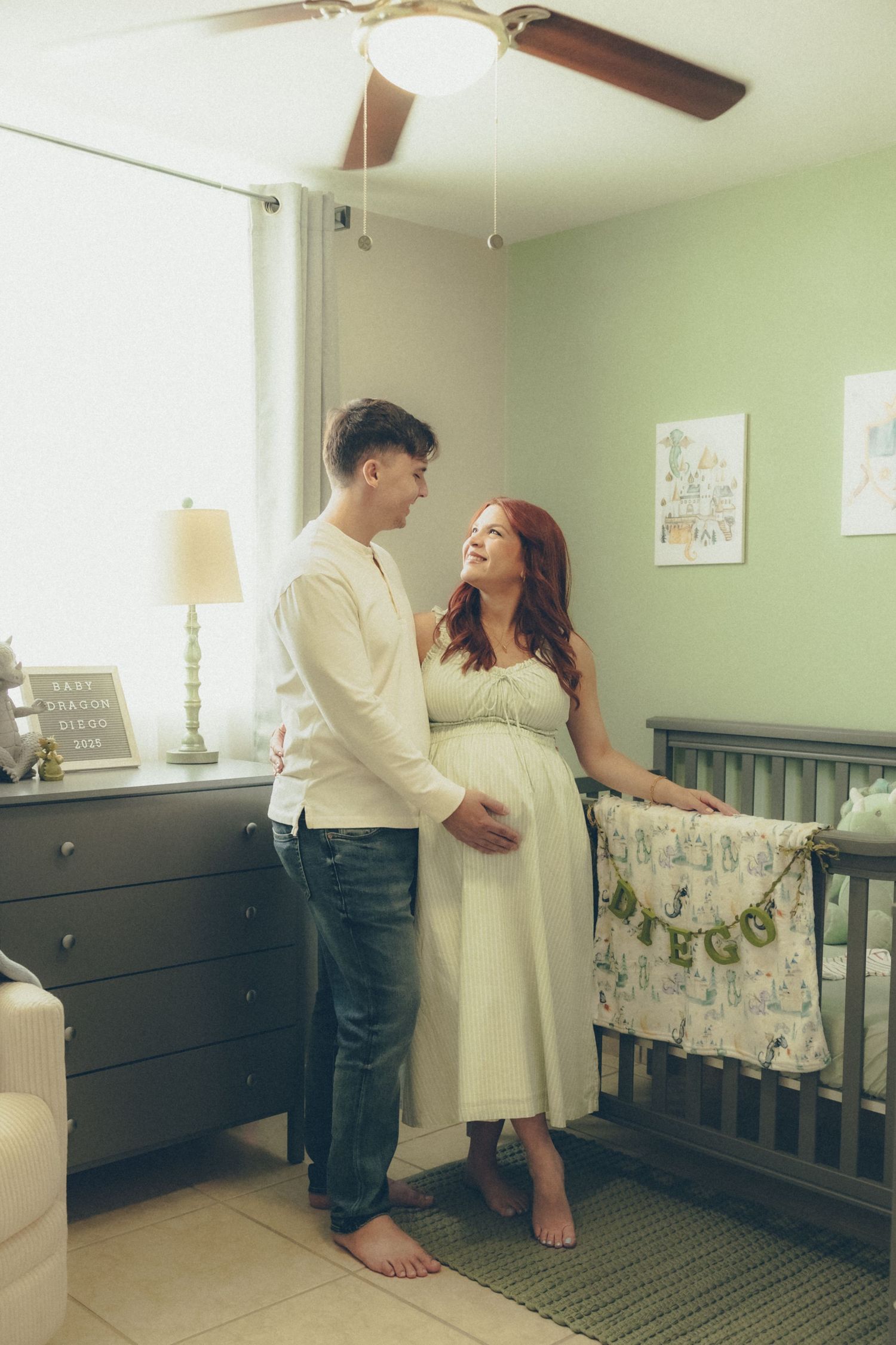 Expecting couple smiling together beside their baby's crib during an at-home maternity session