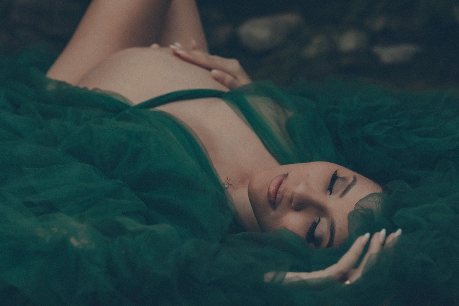 Artistic maternity portrait of an expecting mother lying in layers of flowing green fabric