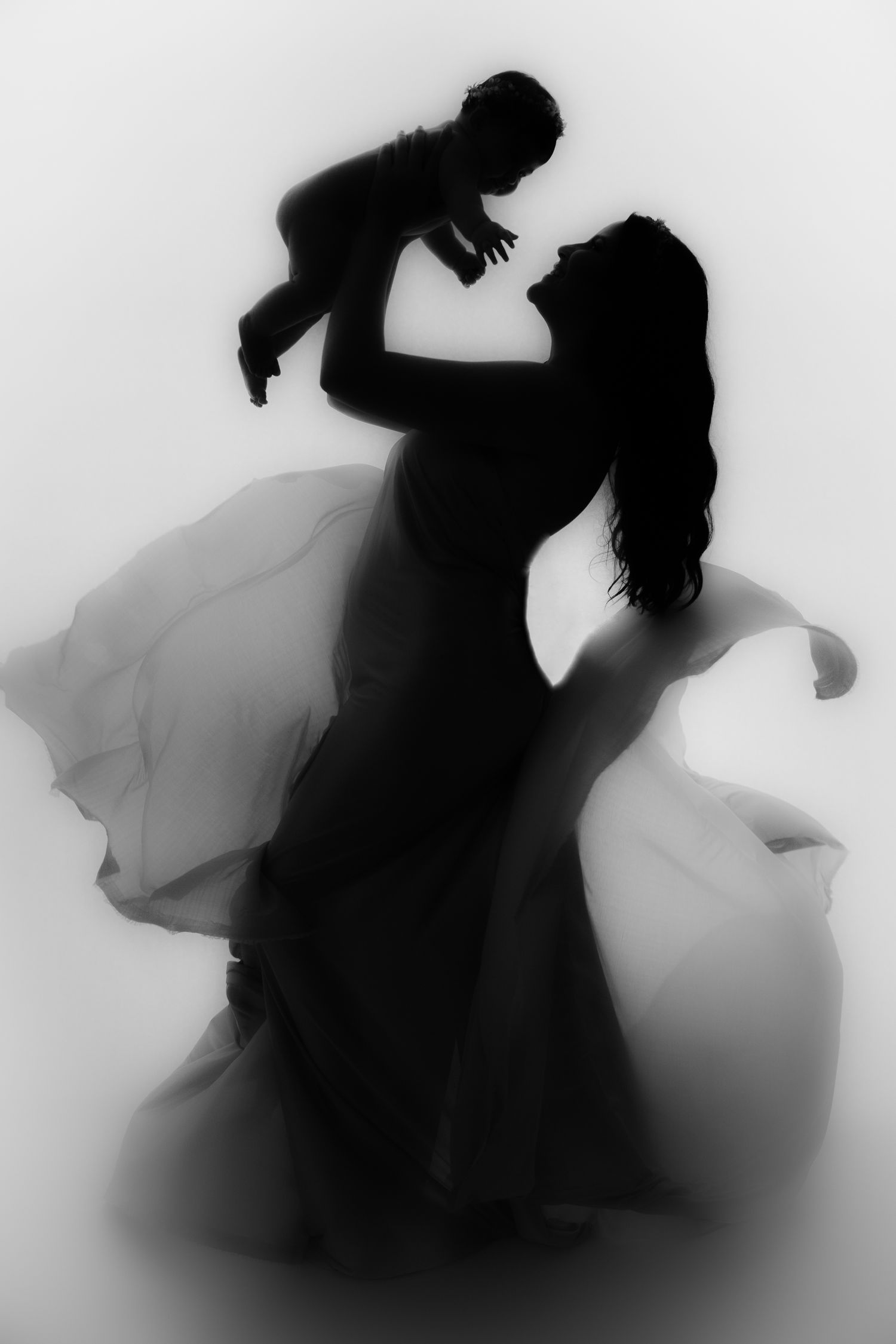Black and white silhouette of a mother lifting her baby into the air during an artistic family portrait