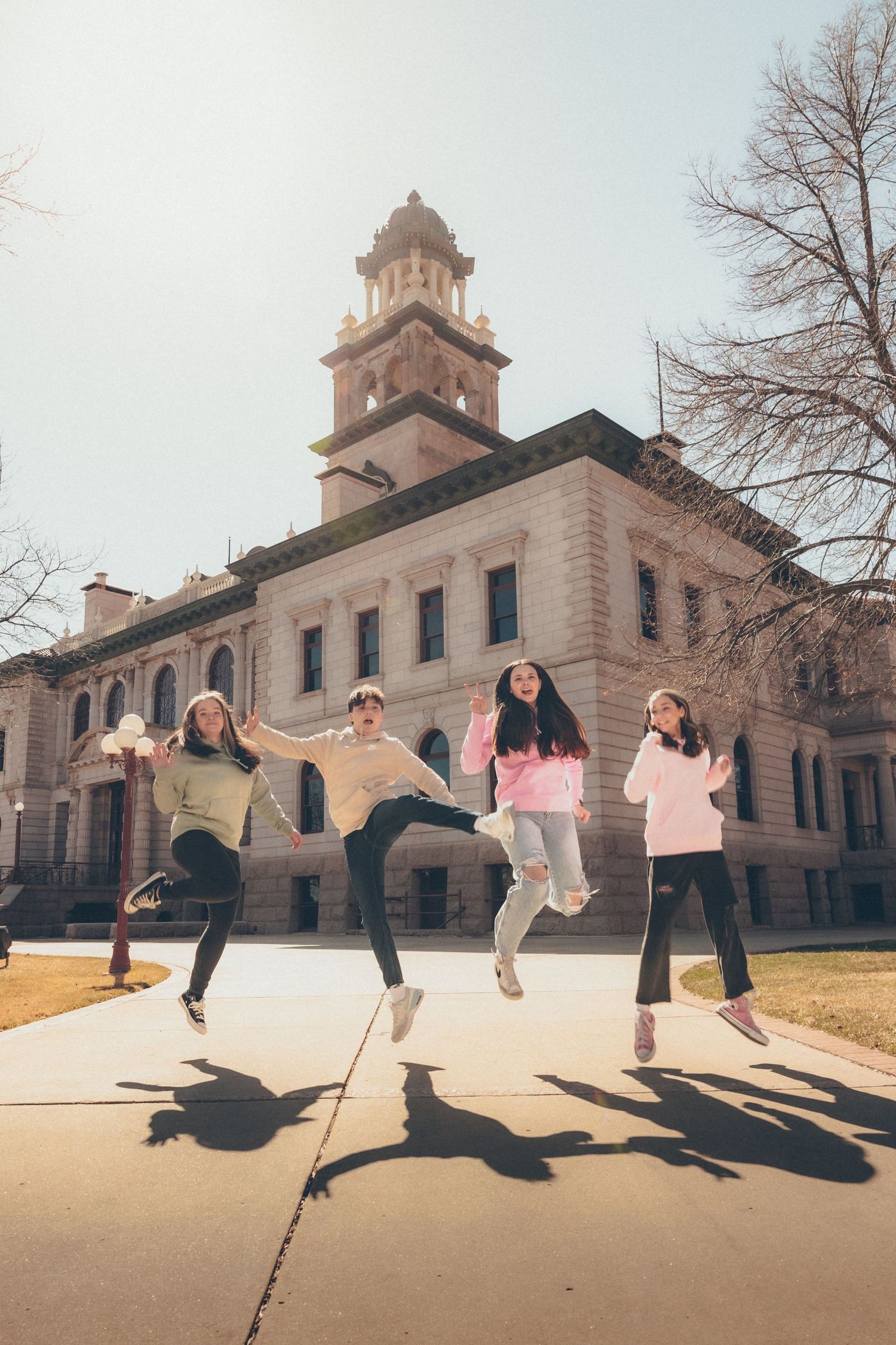 Playful family portrait of four family members jumping together outside a historic building