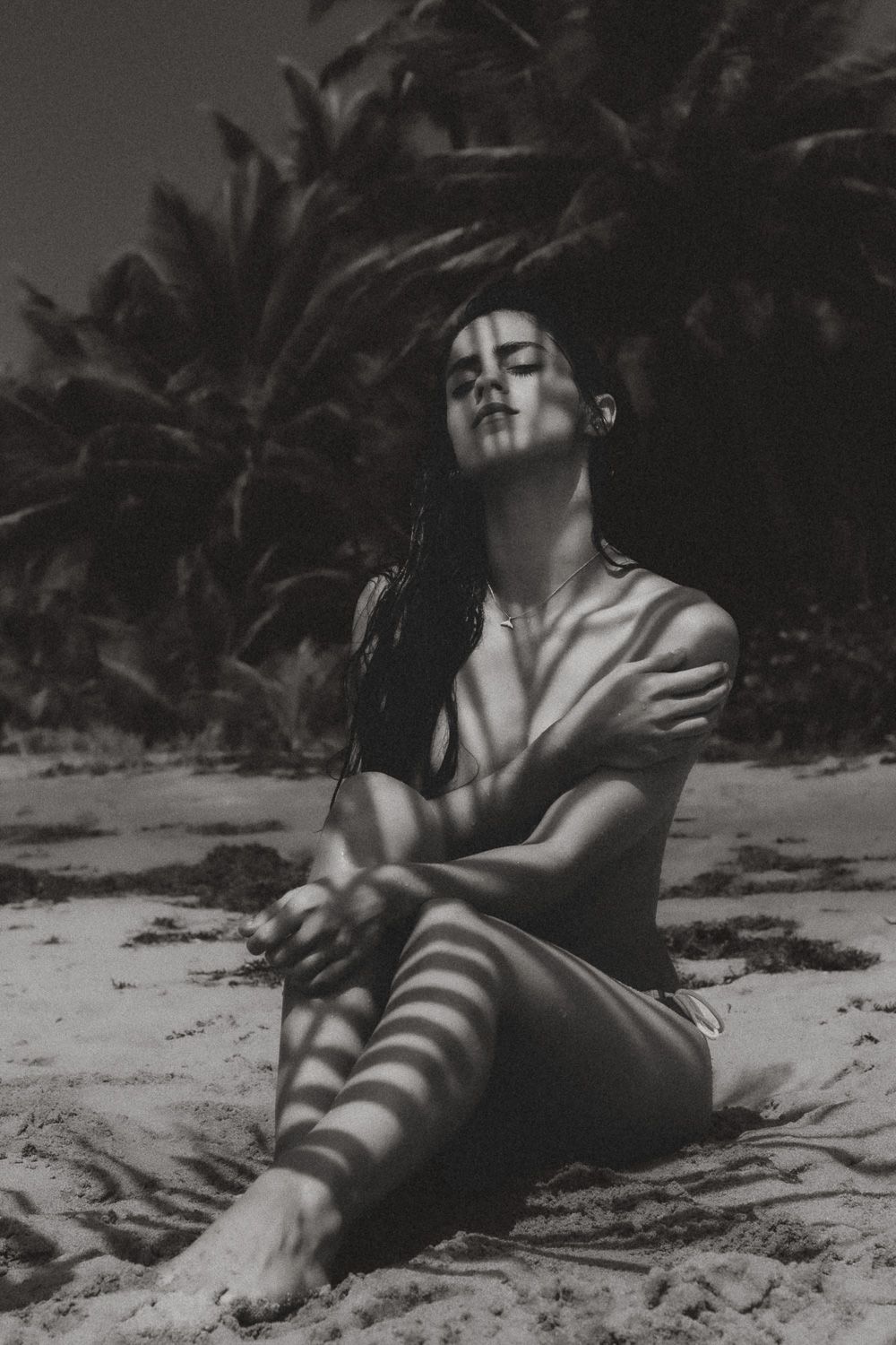 Black and white beach portrait of brunette model with dramatic palm leaf shadows across her body