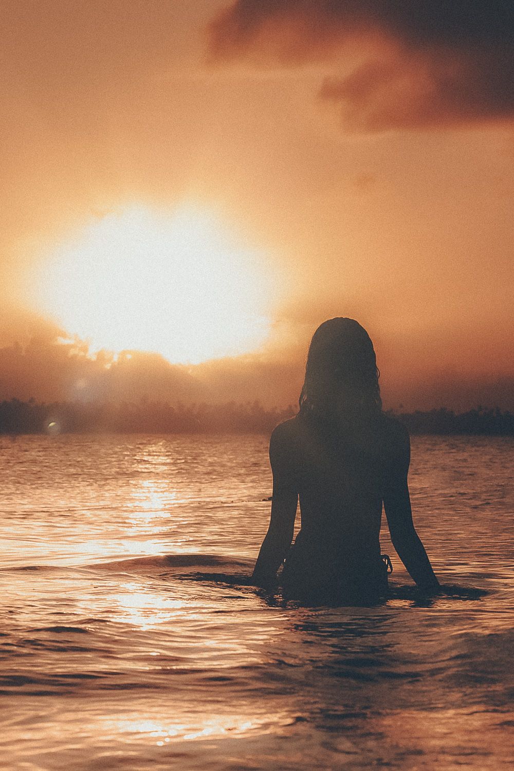 Cinematic silhouette of female model standing in ocean water during a dramatic sunset