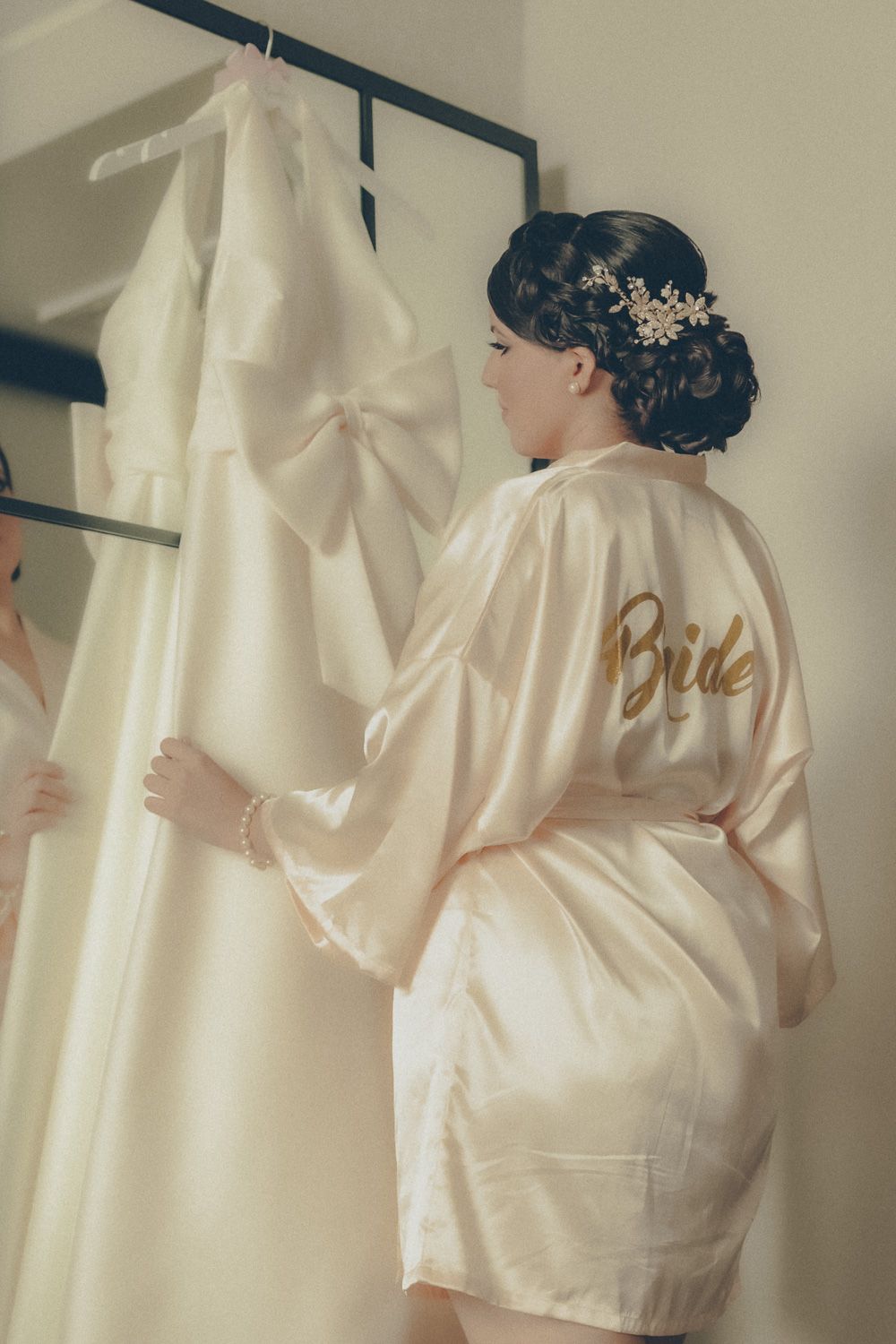 Bride in satin robe looking at her wedding dress while getting ready