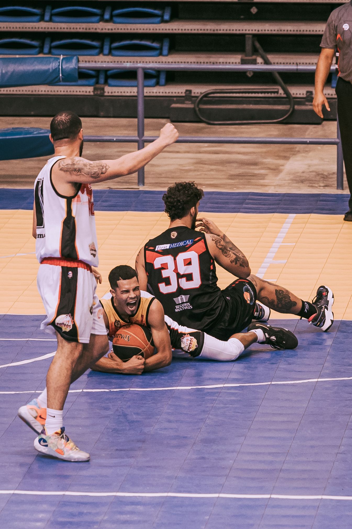 Basketball players compete for a loose ball on the court, with player number 39 in black uniform involved in a scramble.