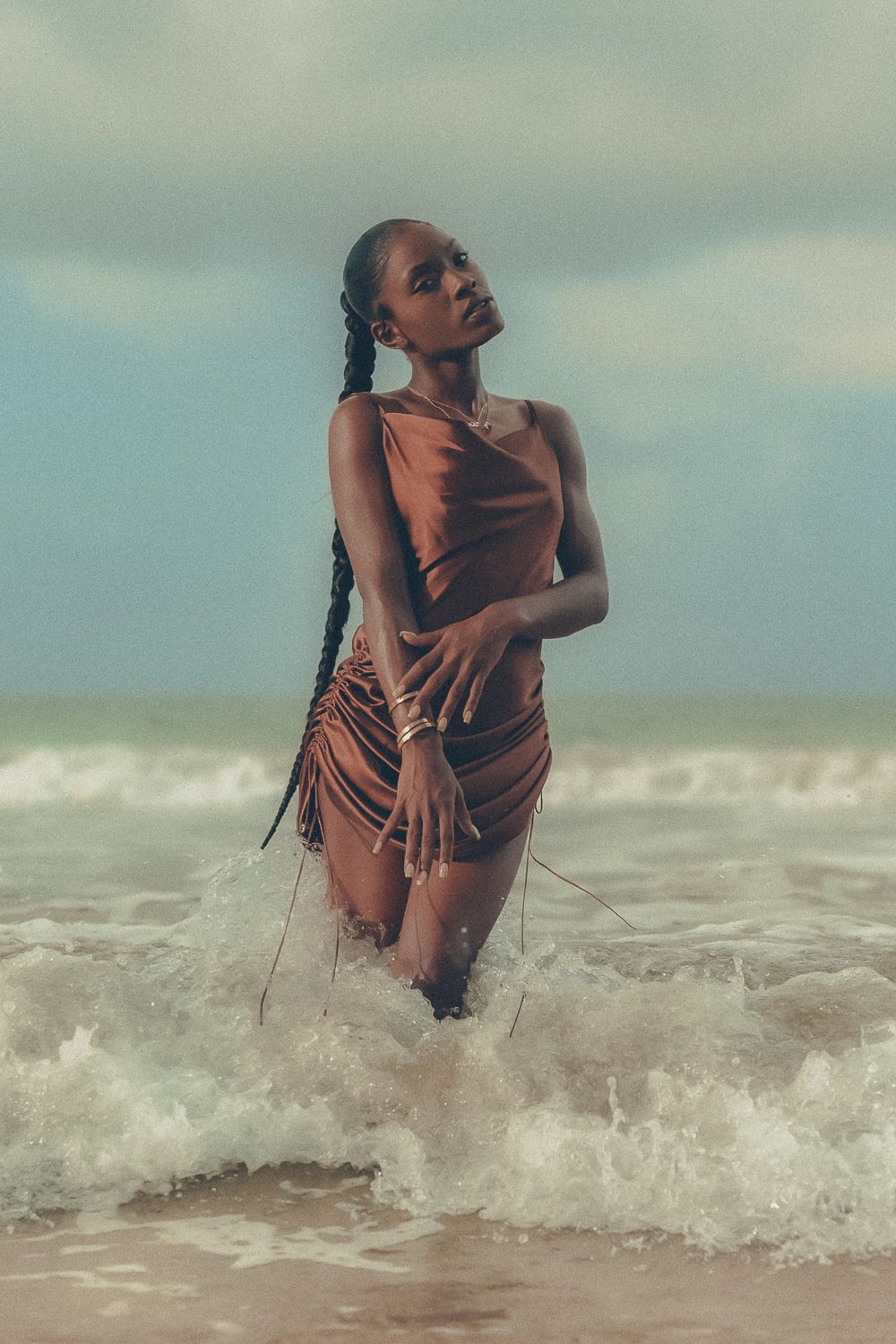 Editorial birthday portrait of a woman in a satin brown dress posing with the beach as the background