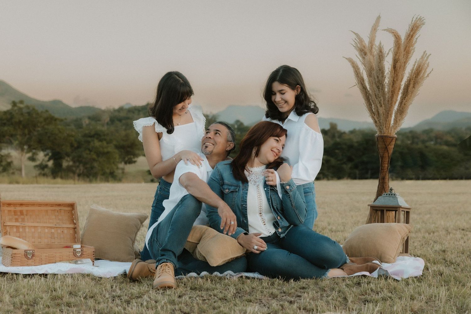 Candid family portrait of parents and their two daughters laughing together during an outdoor picnic session