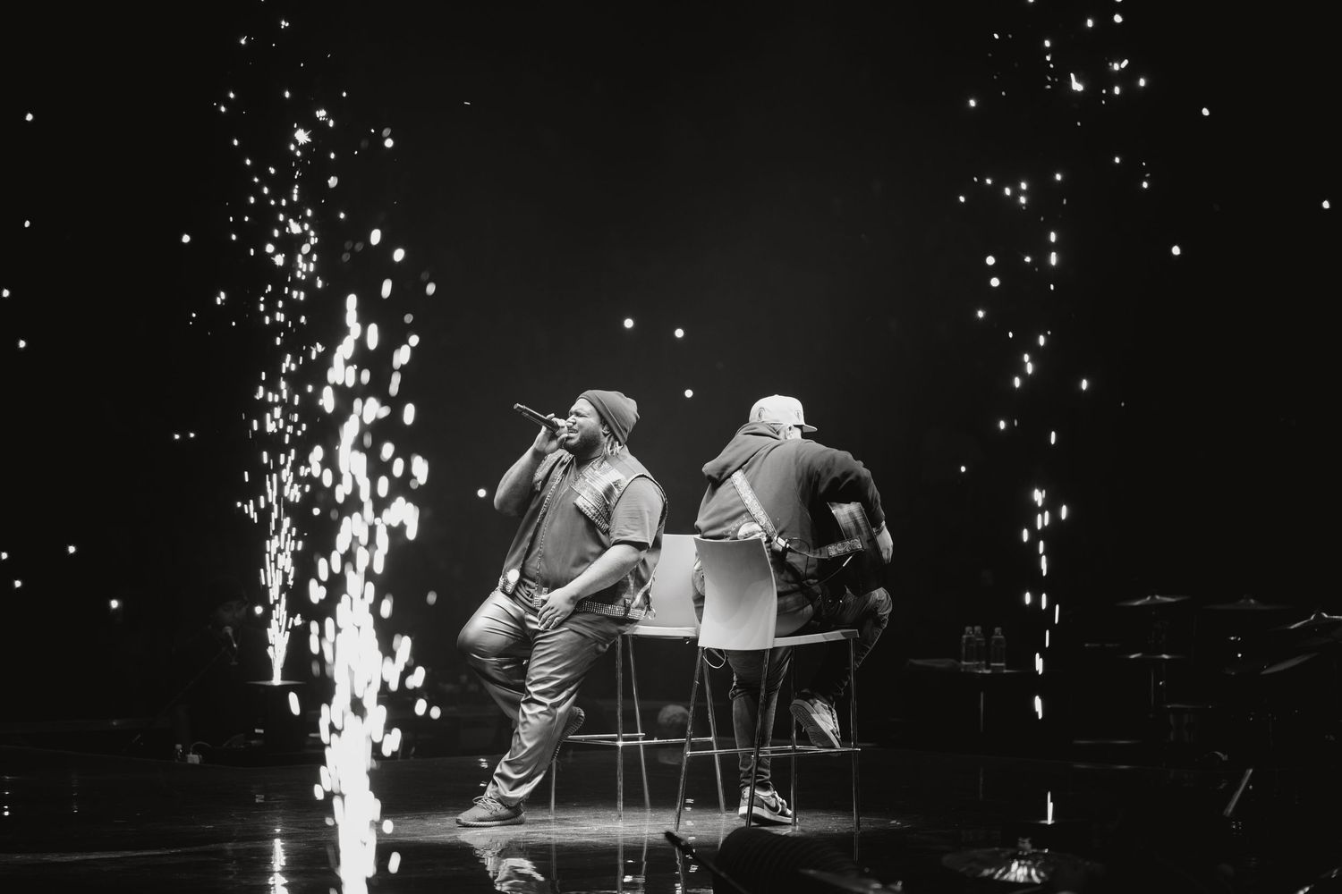 Two performers on stage with pyrotechnic sparks in black and white concert photography.
