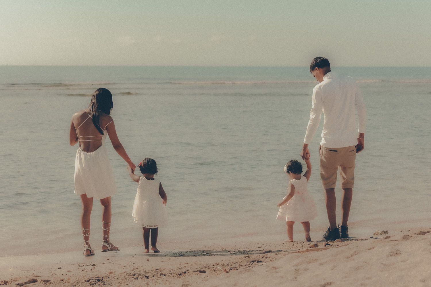 Family of four walking hand in hand along the beach with their two young children beside the ocean