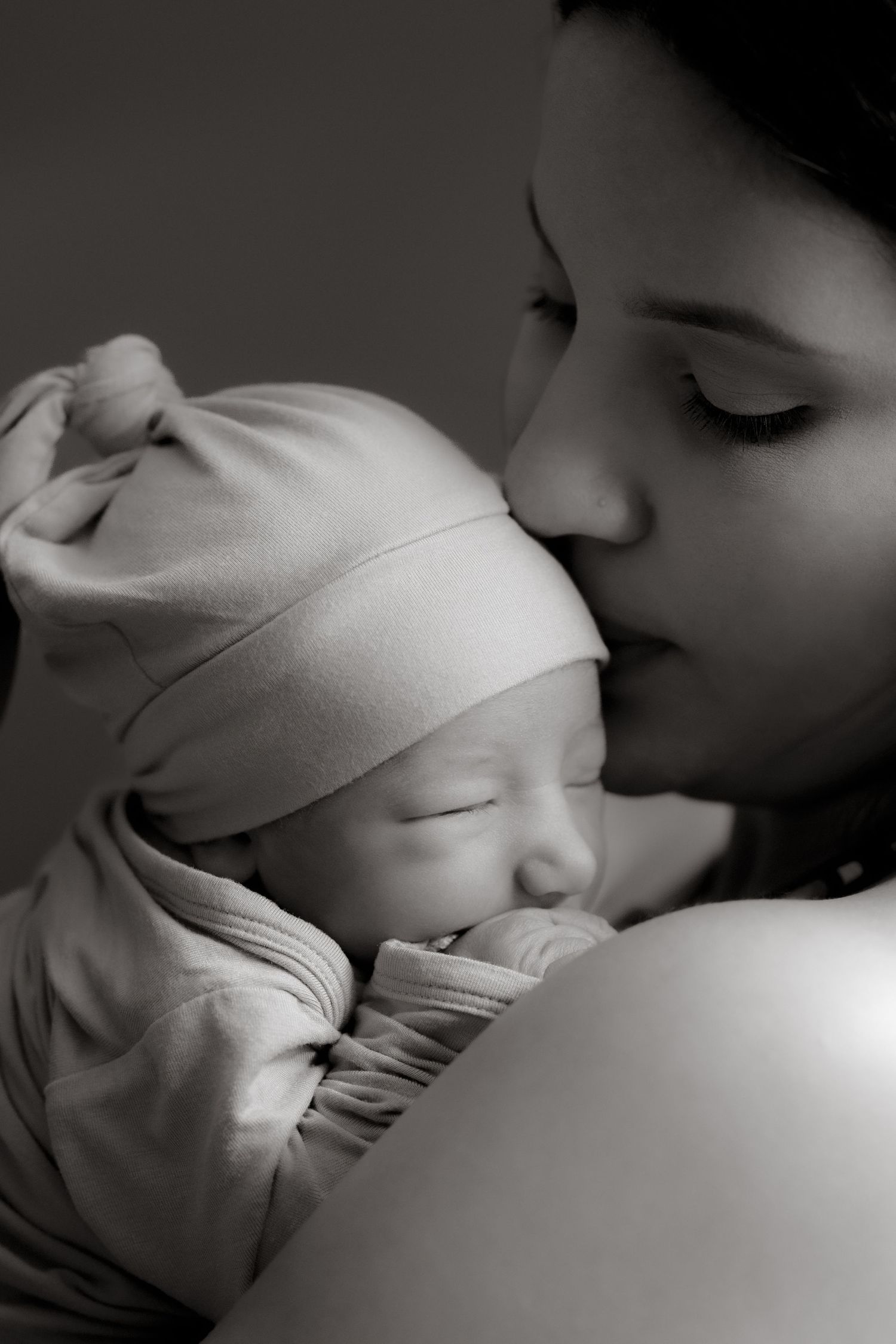 Black and white close-up of a sleeping newborn baby being gently kissed during an intimate family session