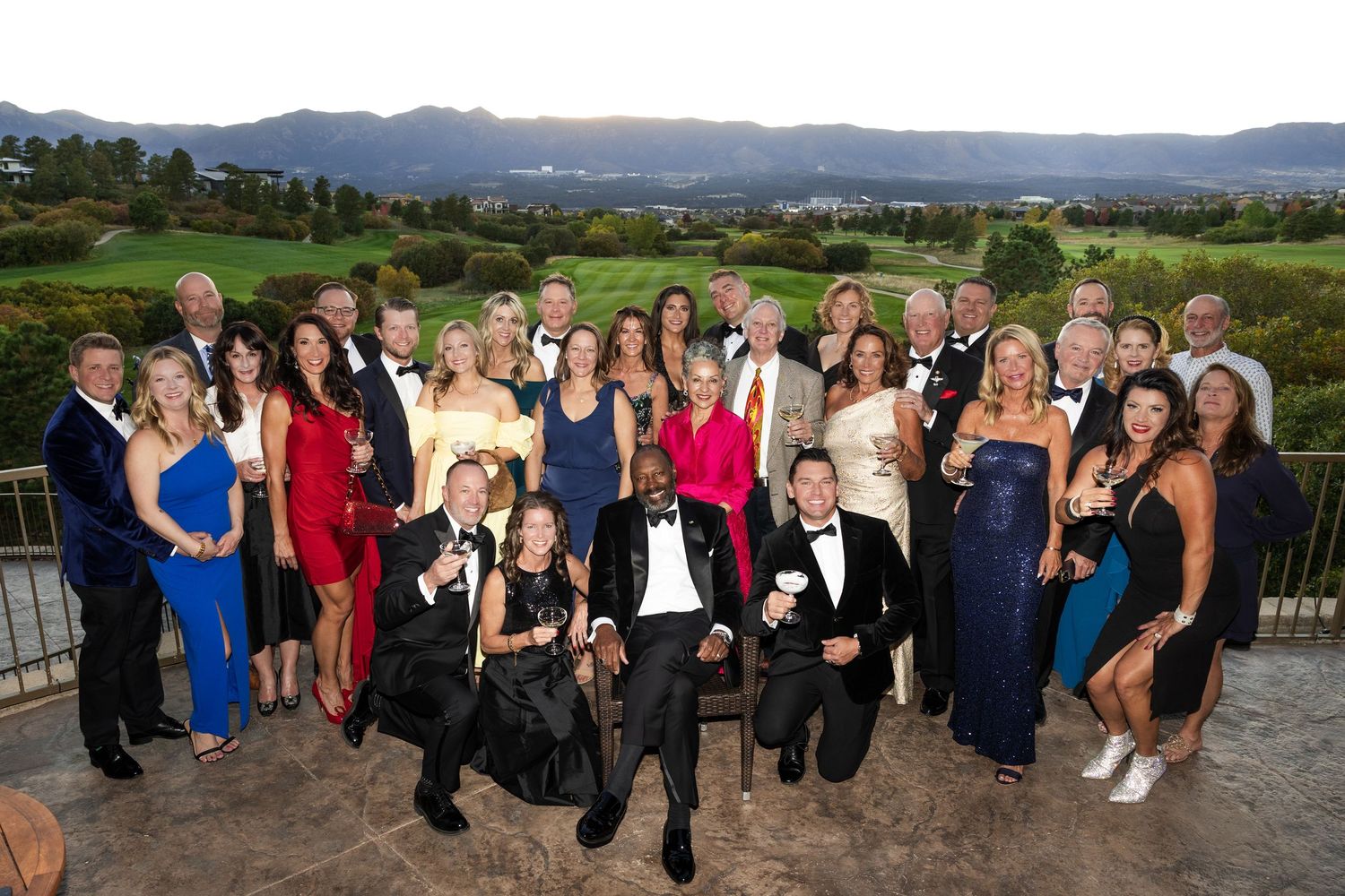Large group of elegantly dressed guests posing together at a formal outdoor gala event with scenic golf course views.