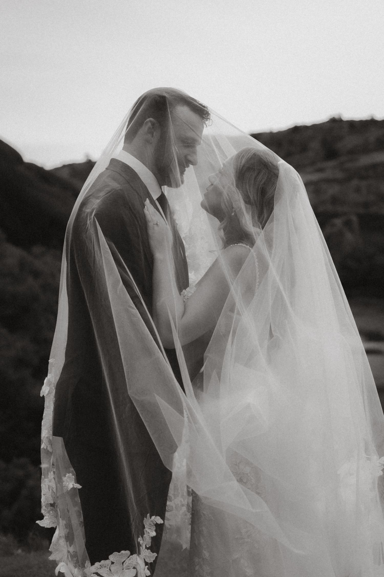 Black and white image of the bride and groom looking at each other eyes under the wedding vail