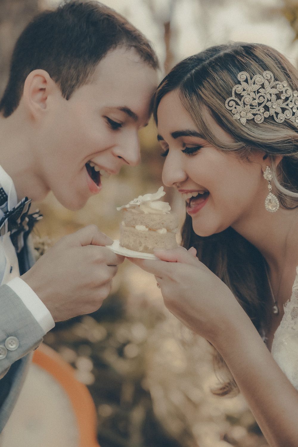 Bride and groom laughing while sharing wedding cake outdoors