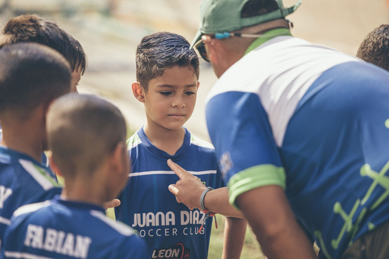Youth soccer players in blue Juana Diaz Soccer Club jerseys receive coaching instructions during a match.