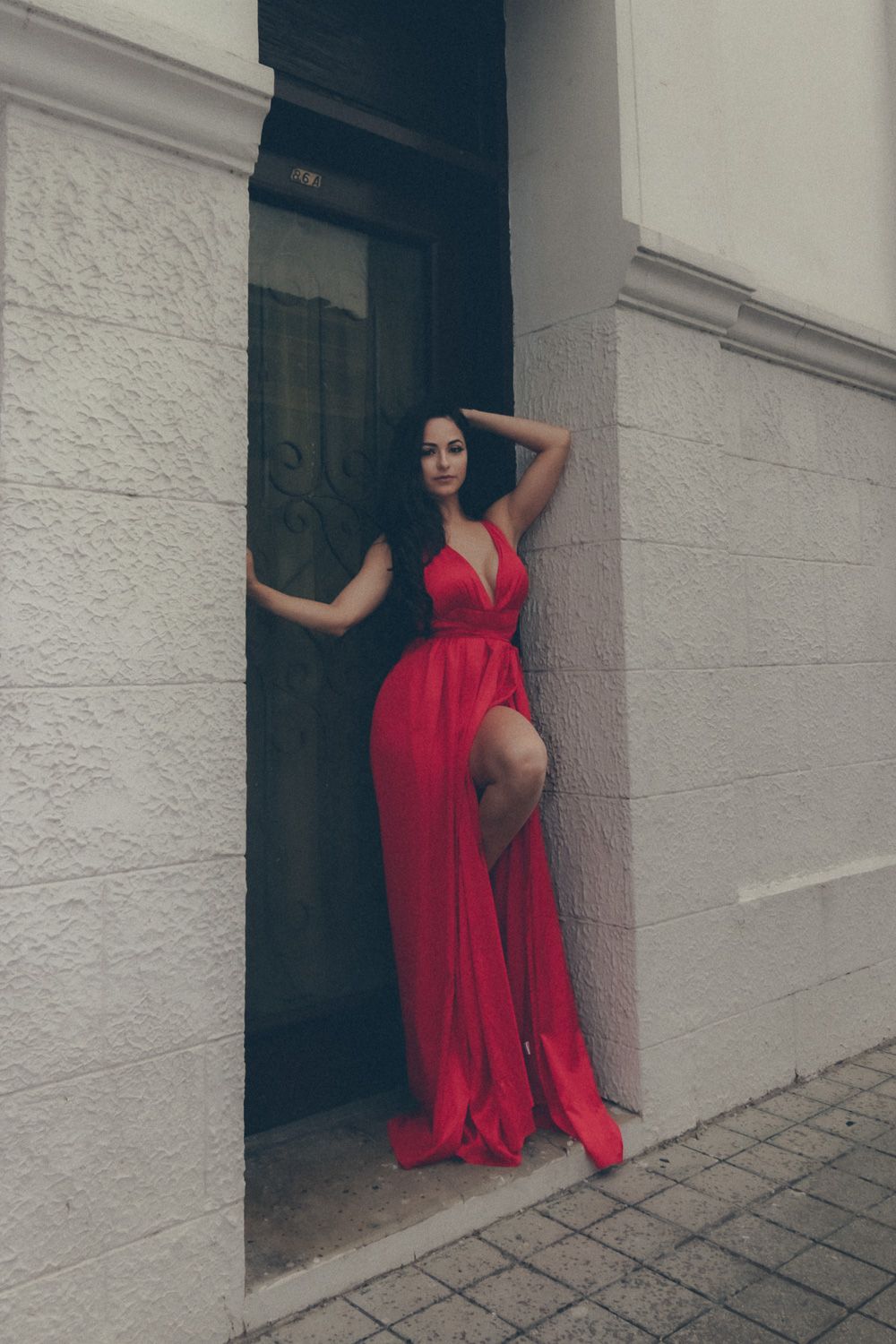 Elegant birthday portrait of a woman in a red dress posing confidently in an architectural doorway