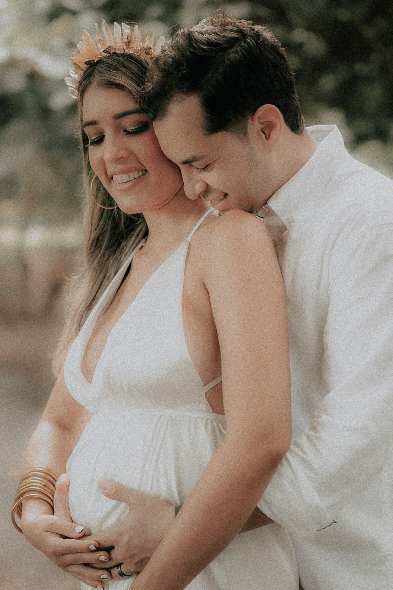 Expecting couple embracing and smiling together during an outdoor maternity photoshoot