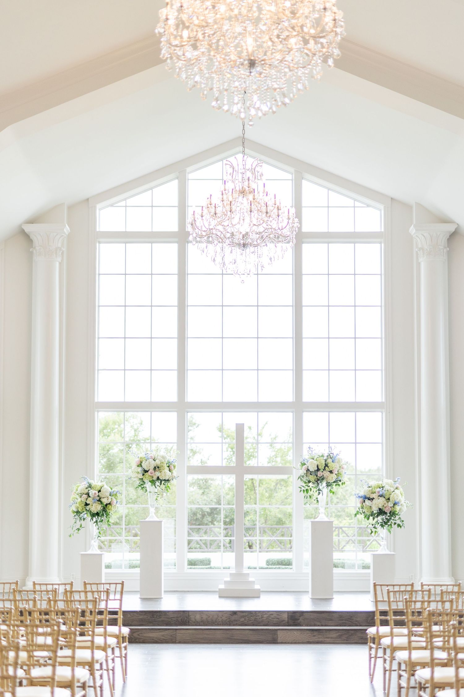 Bright white wedding chapel featuring vaulted ceiling, crystal chandelier, and floral altar arrangements.