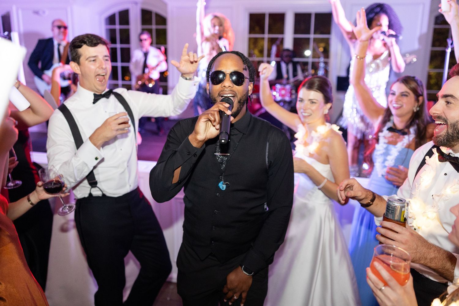 Energetic performer sings into microphone at lively wedding reception with dancing guests.