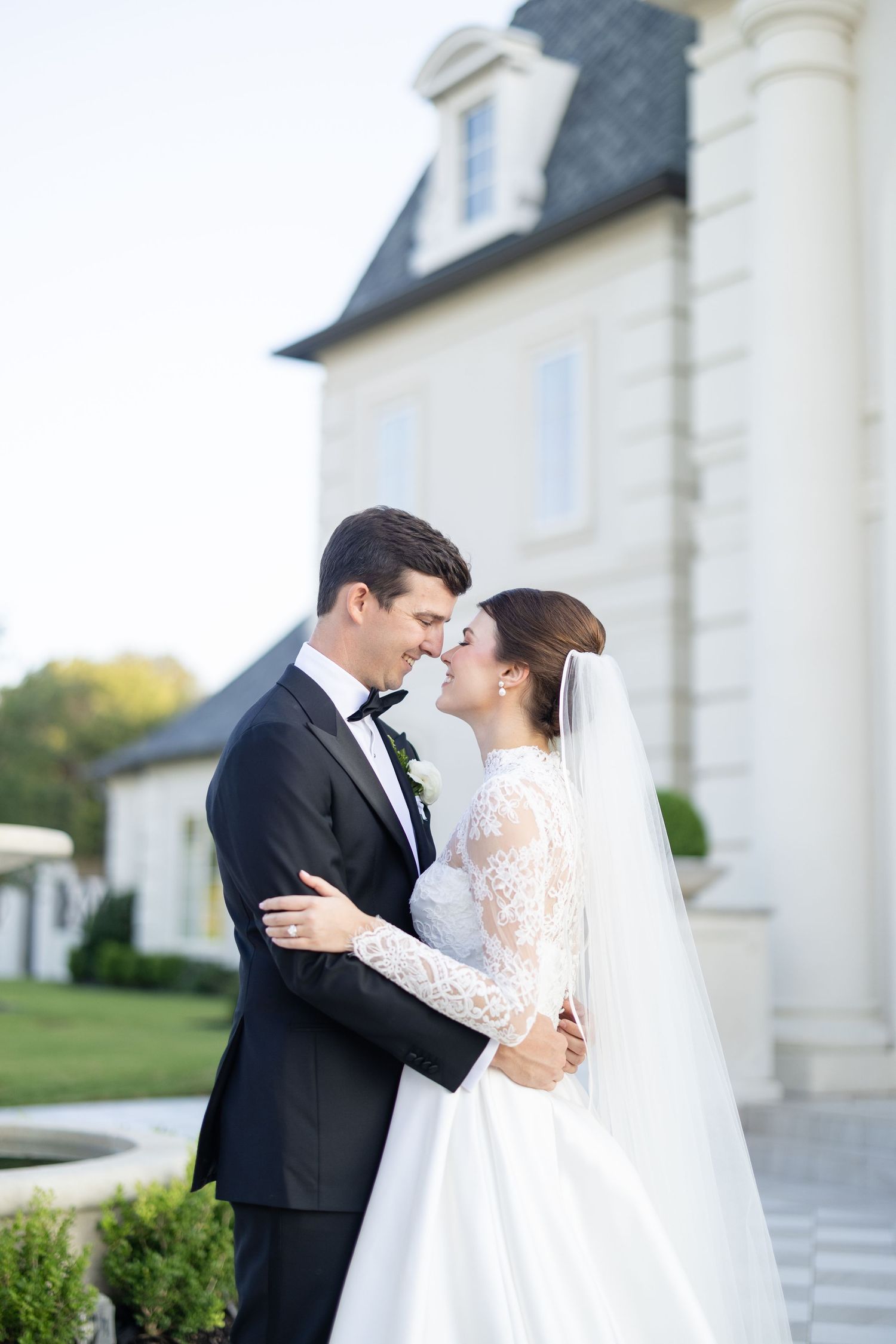 Bride and groom sharing a romantic almost-kiss moment outside a beautiful white chateau estate.