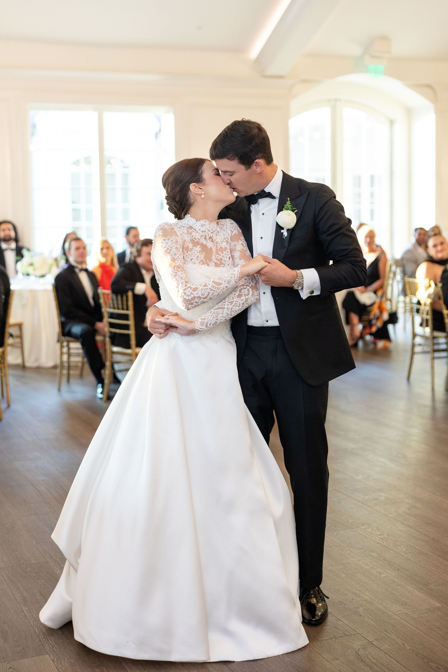Bride and groom share a tender kiss during their first dance in an elegant white wedding reception venue.