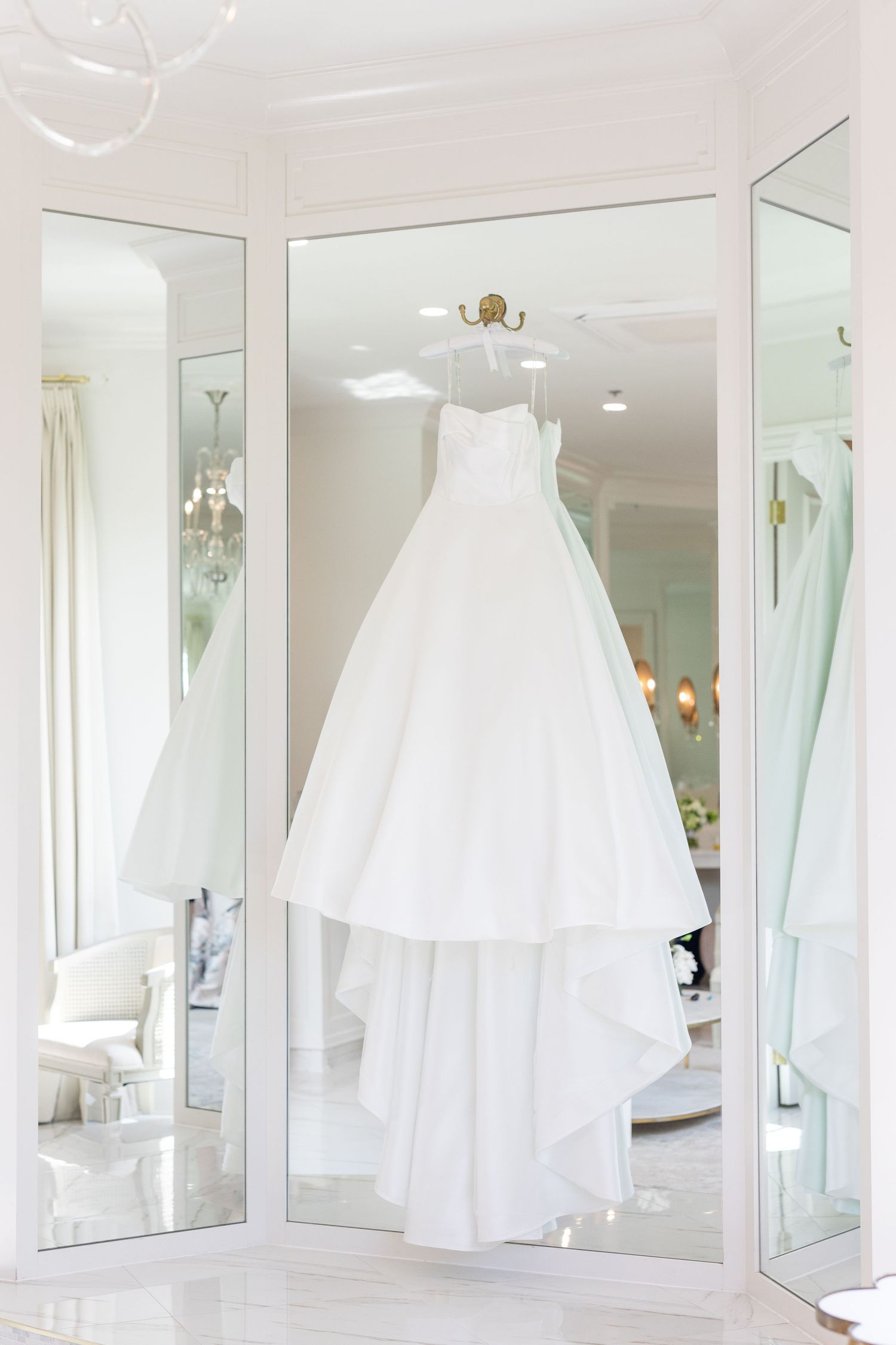 Elegant white ball gown wedding dress hanging between mirrored closet doors in bright bridal suite.