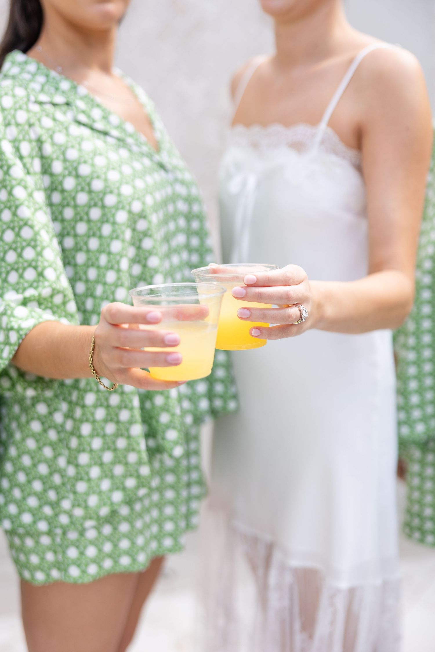Two women in getting-ready attire clink glasses of orange juice during pre-wedding bridal preparations.