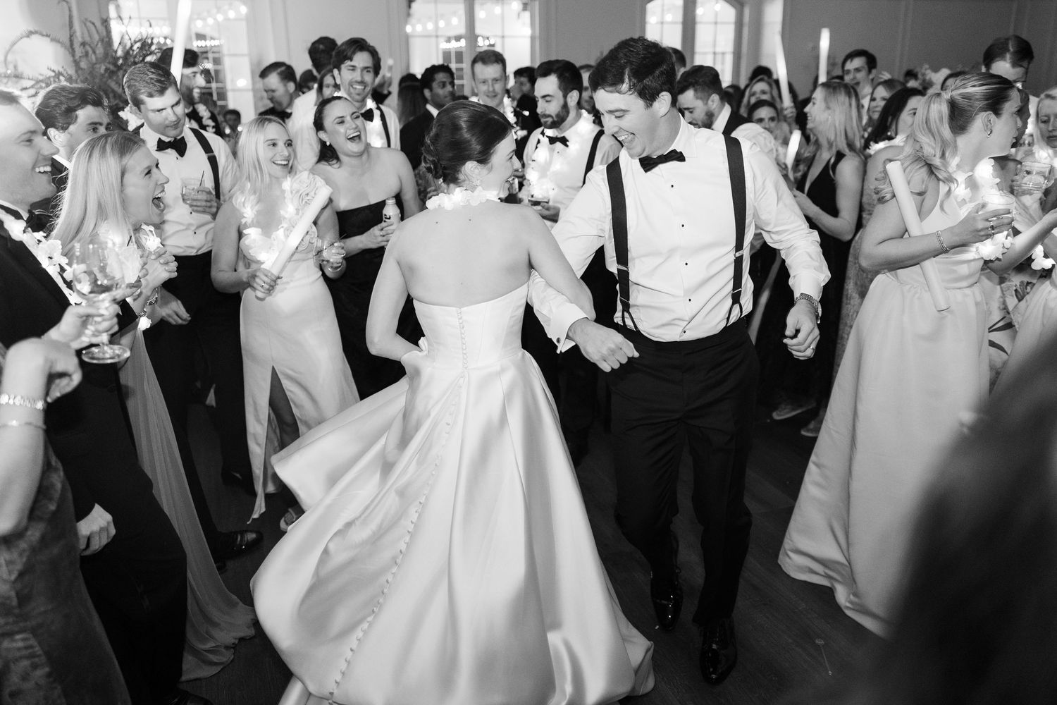 Bride and groom dance energetically surrounded by wedding guests in black and white photo.