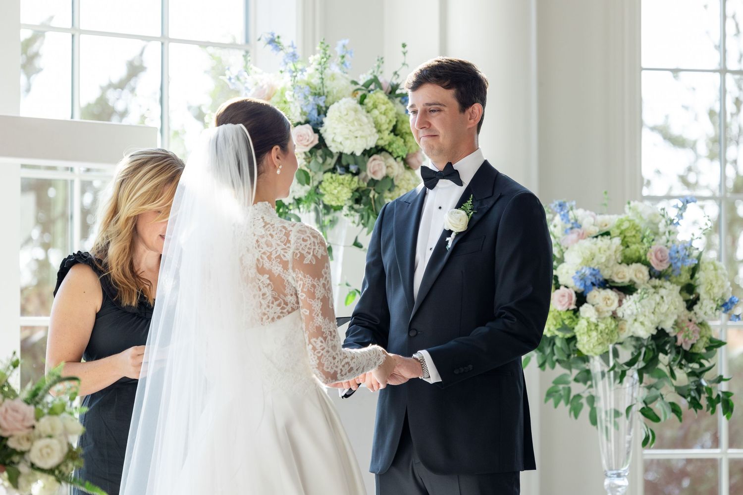 Bride and groom exchanging vows at the altar with blue and white floral arrangements in the background.