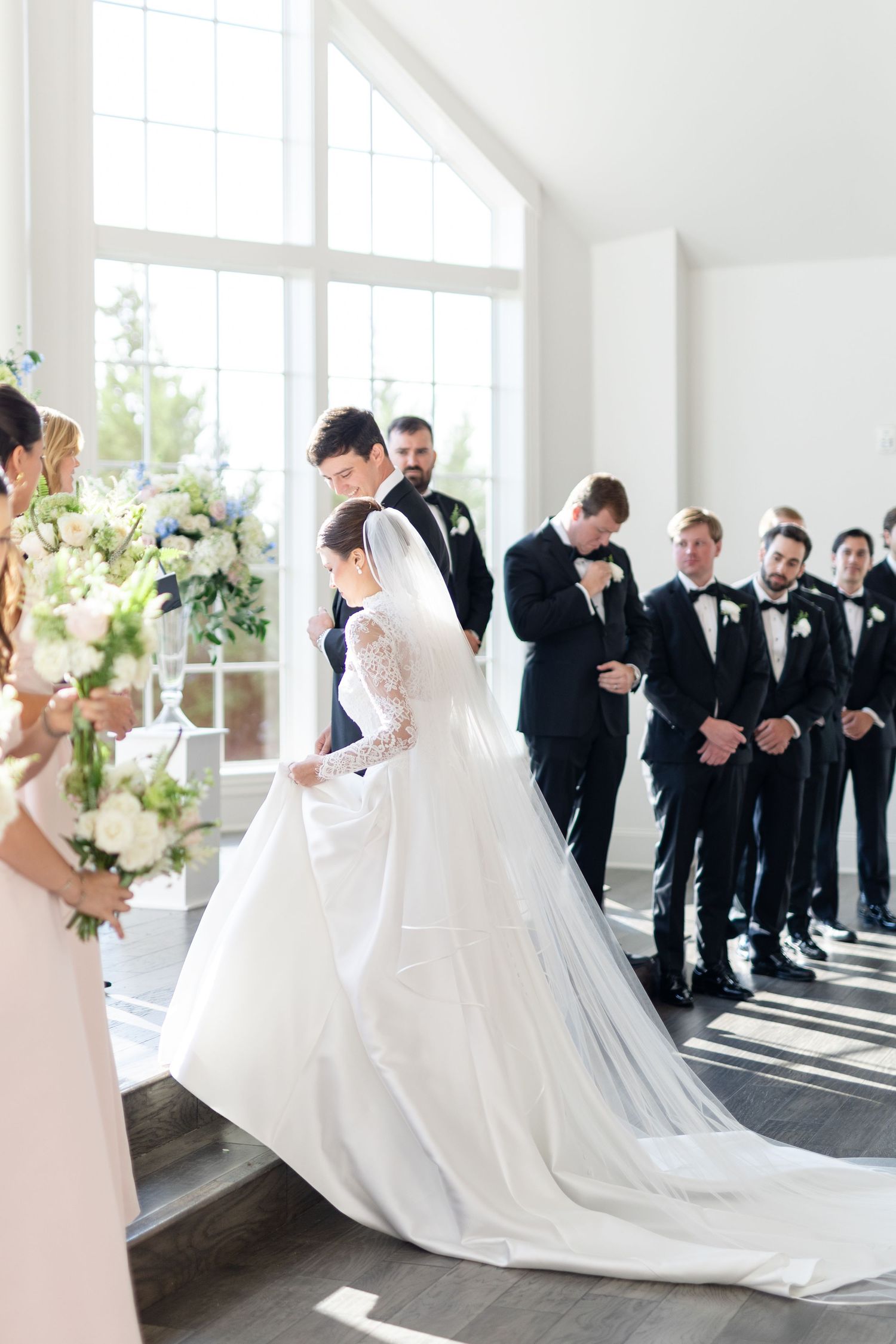 Bride in a long white gown with veil and groom in black tuxedo at the wedding ceremony altar.