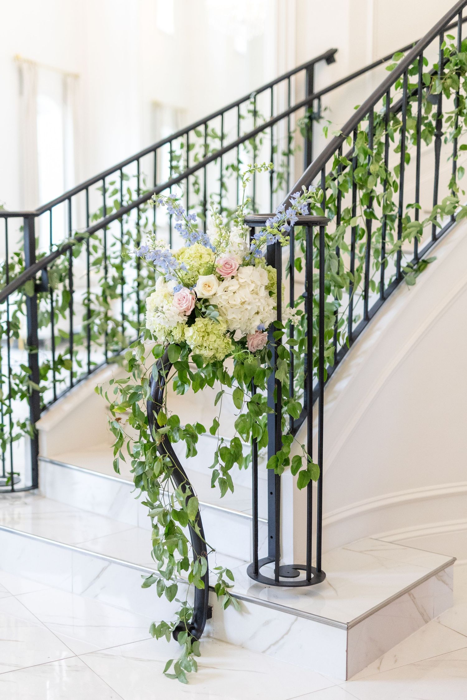 Elegant staircase railing adorned with lush greenery and white, pink, and blue floral wedding decorations.