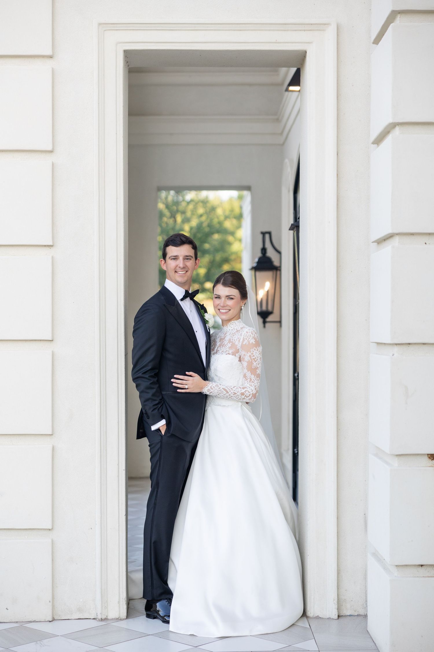 Elegant bride and groom posing together in a white doorway of a classic wedding venue.