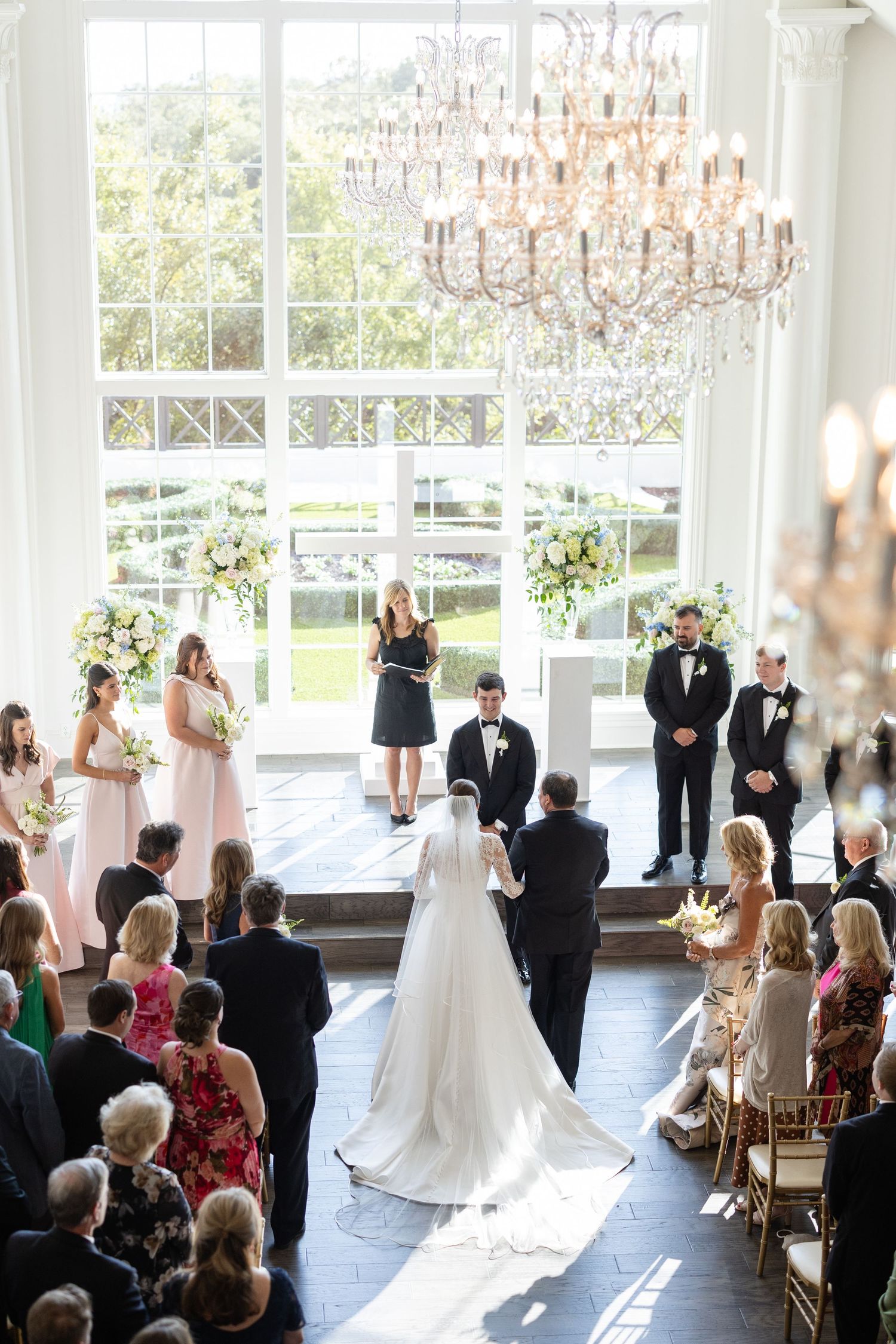 Aerial view of a wedding ceremony with bride and groom at the altar beneath a crystal chandelier.