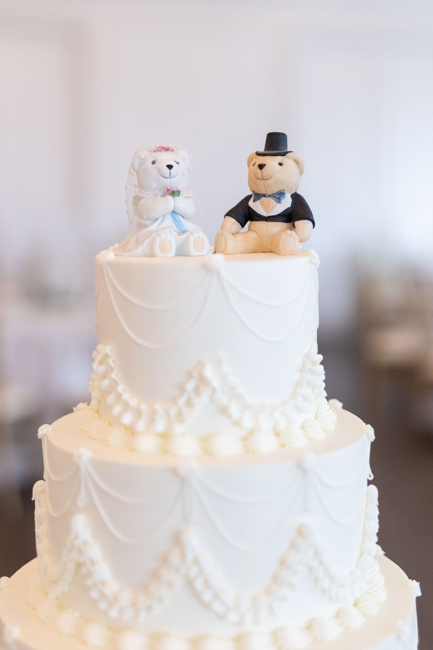 Close-up of adorable teddy bear bride and groom cake toppers on white pearl-decorated wedding cake tier.