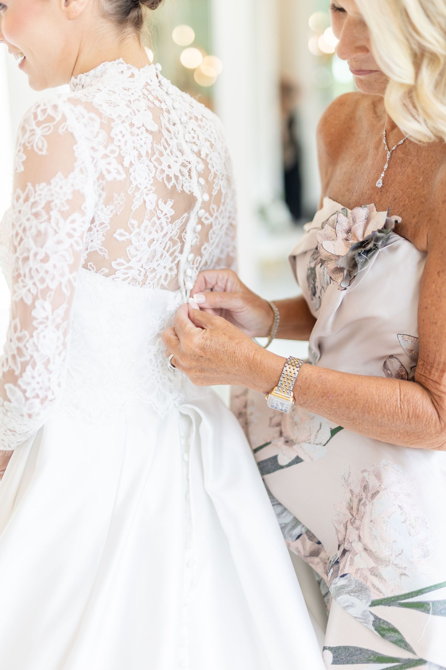 Mother buttoning the back of brides white lace wedding gown before the ceremony.