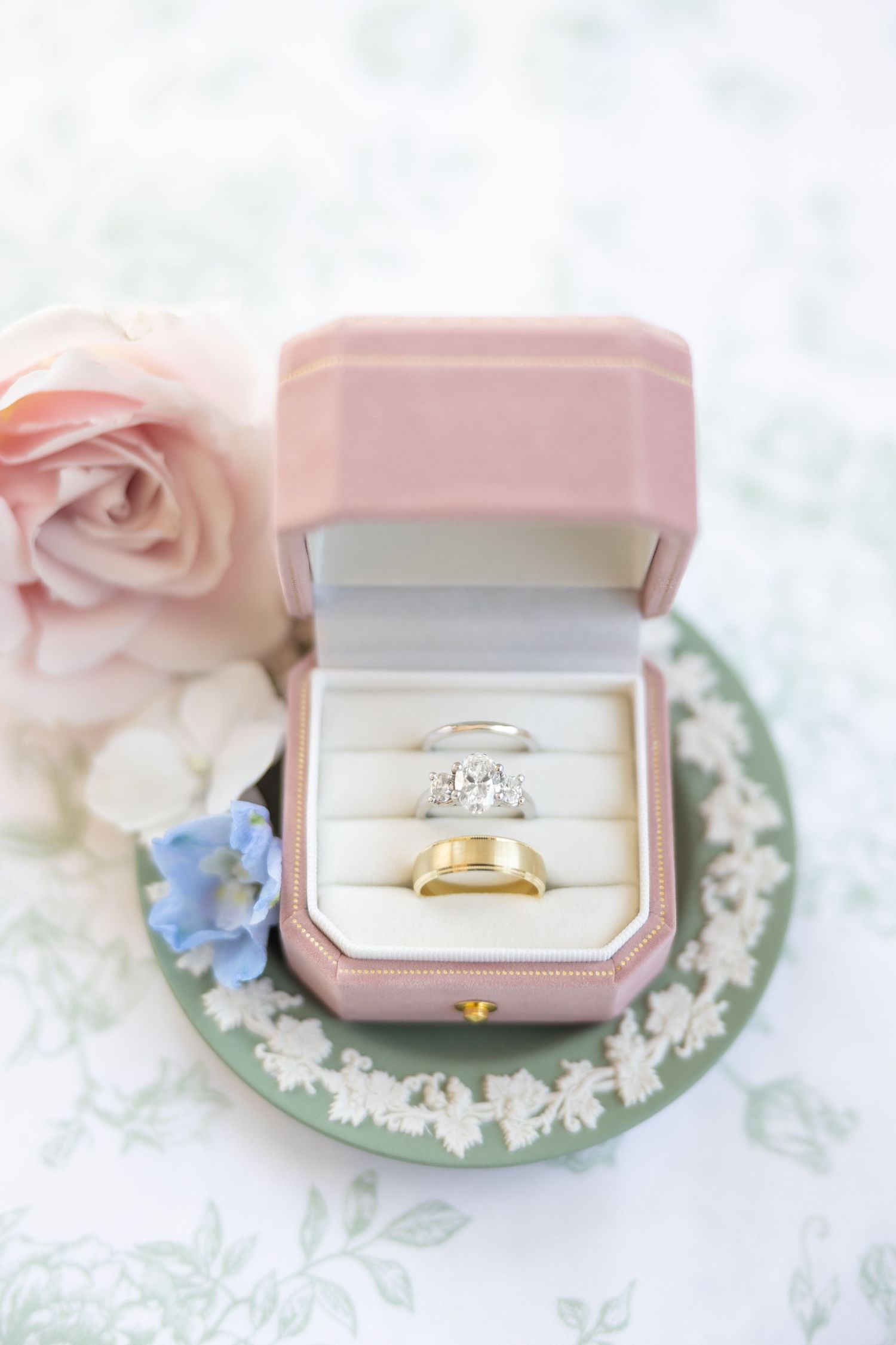 Gold diamond engagement ring and wedding band displayed in pink velvet ring box with roses.