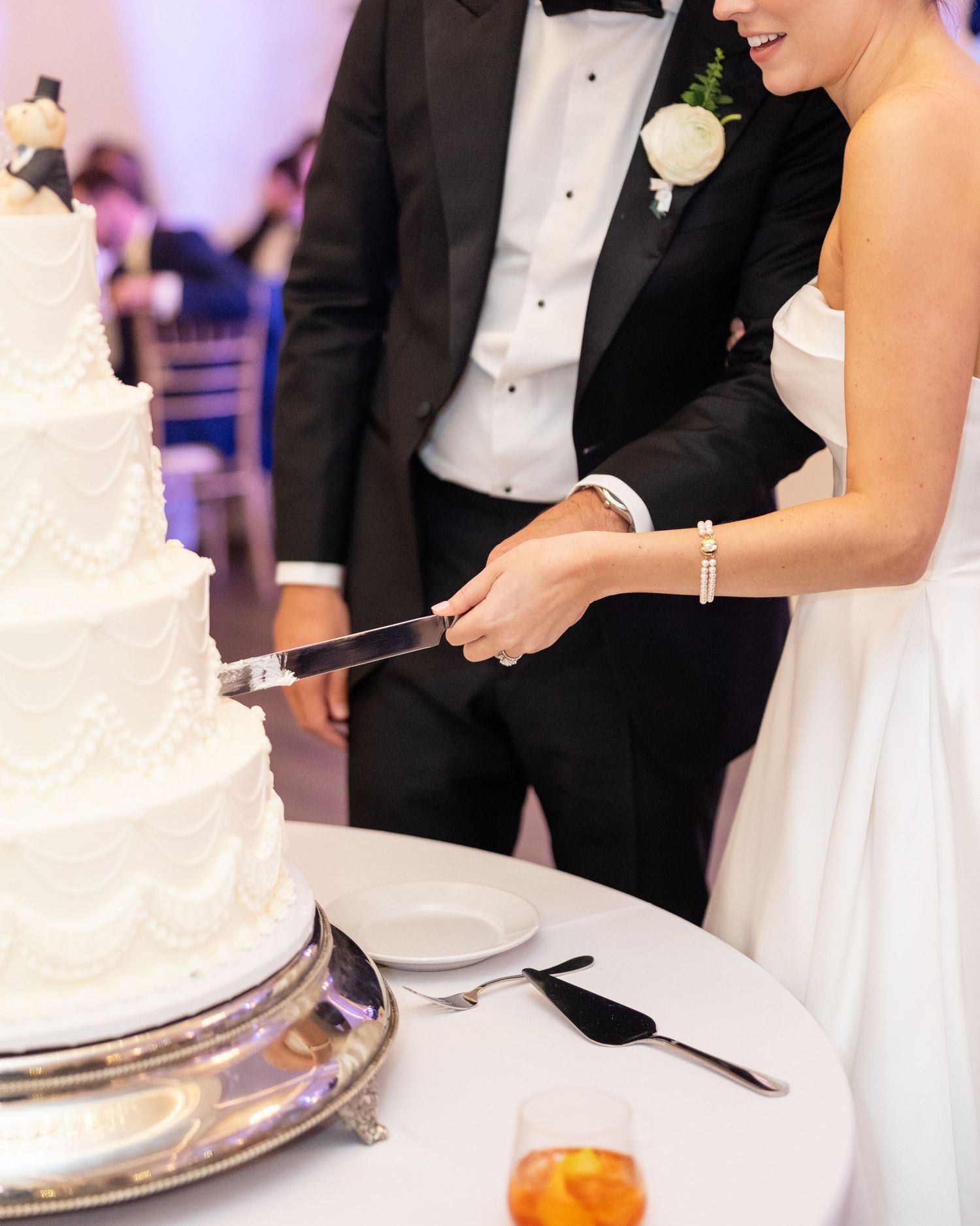 Bride in strapless gown and groom in tuxedo cutting white tiered wedding cake together.