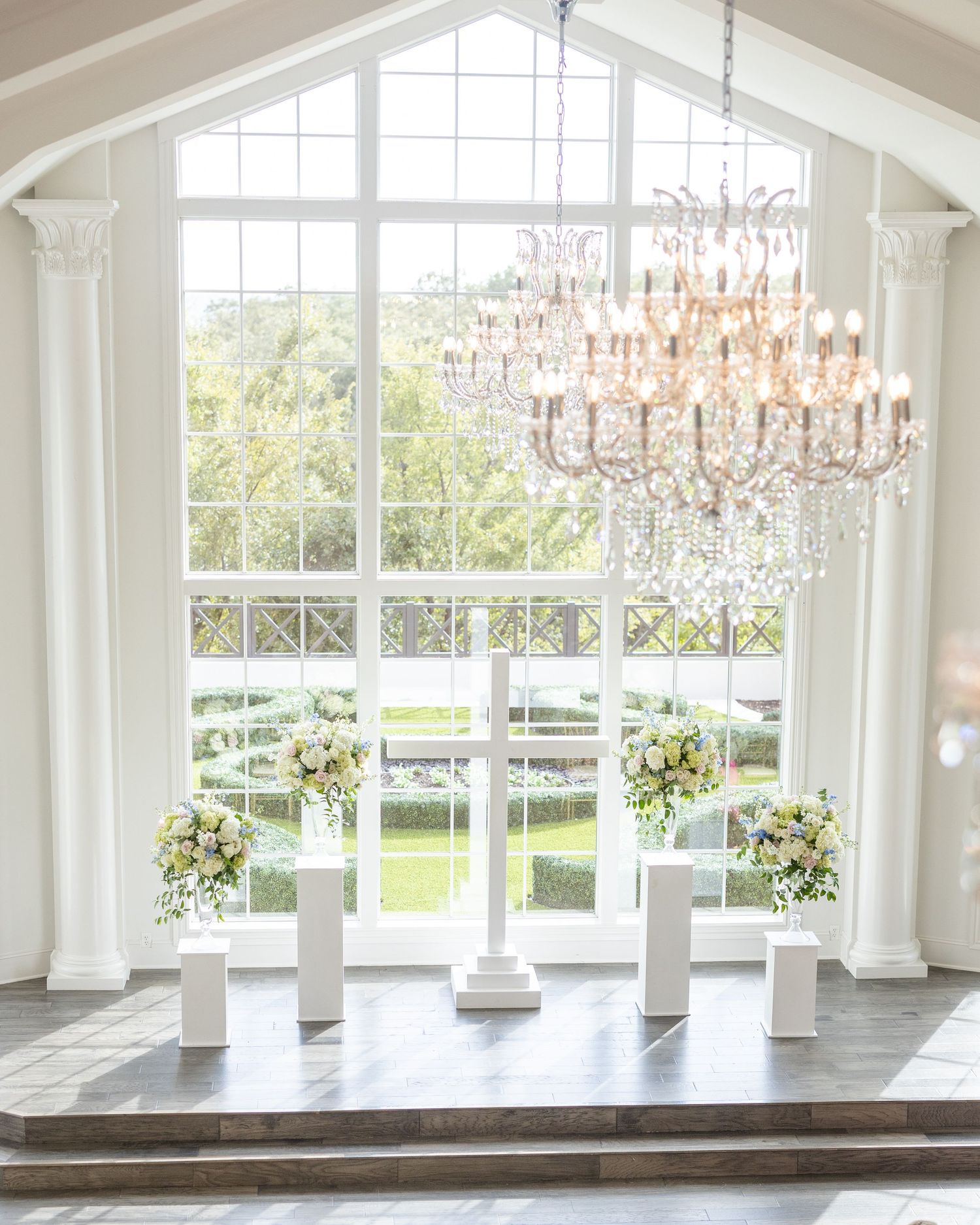 Stunning white wedding chapel altar with crystal chandelier, tall windows, and white floral arrangements.