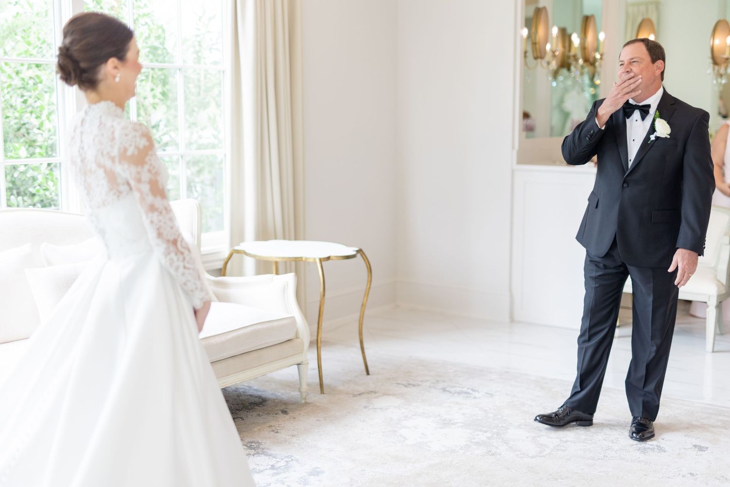 Emotional father wipes tears seeing his daughter in her white lace wedding gown for first look.