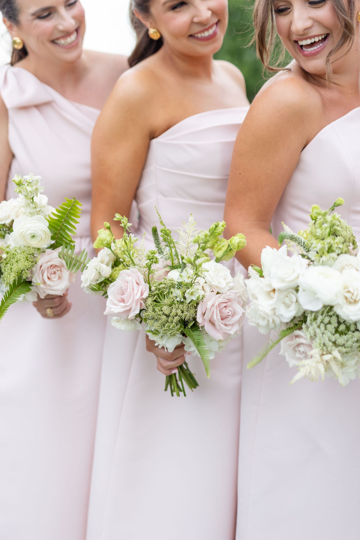 Smiling bridesmaids in blush gowns holding elegant bouquets of pink roses and white flowers.