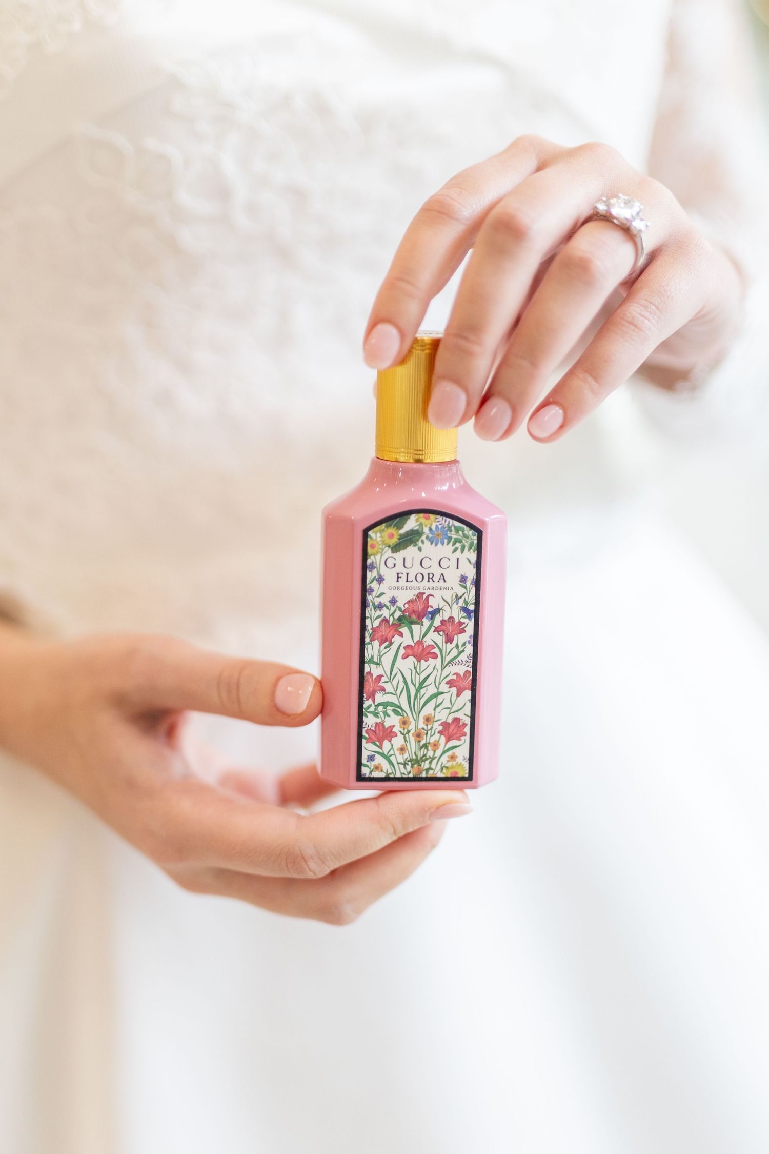 Bride holding Gucci Flora perfume bottle with diamond engagement ring on her finger.