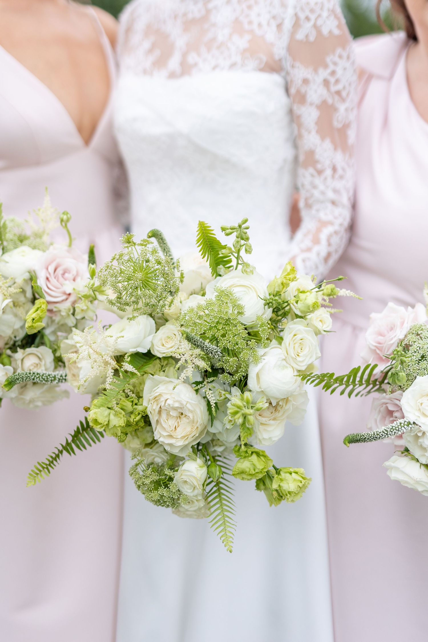 Close-up of lush bridal bouquet with white ranunculus, green ferns, and soft pink roses.