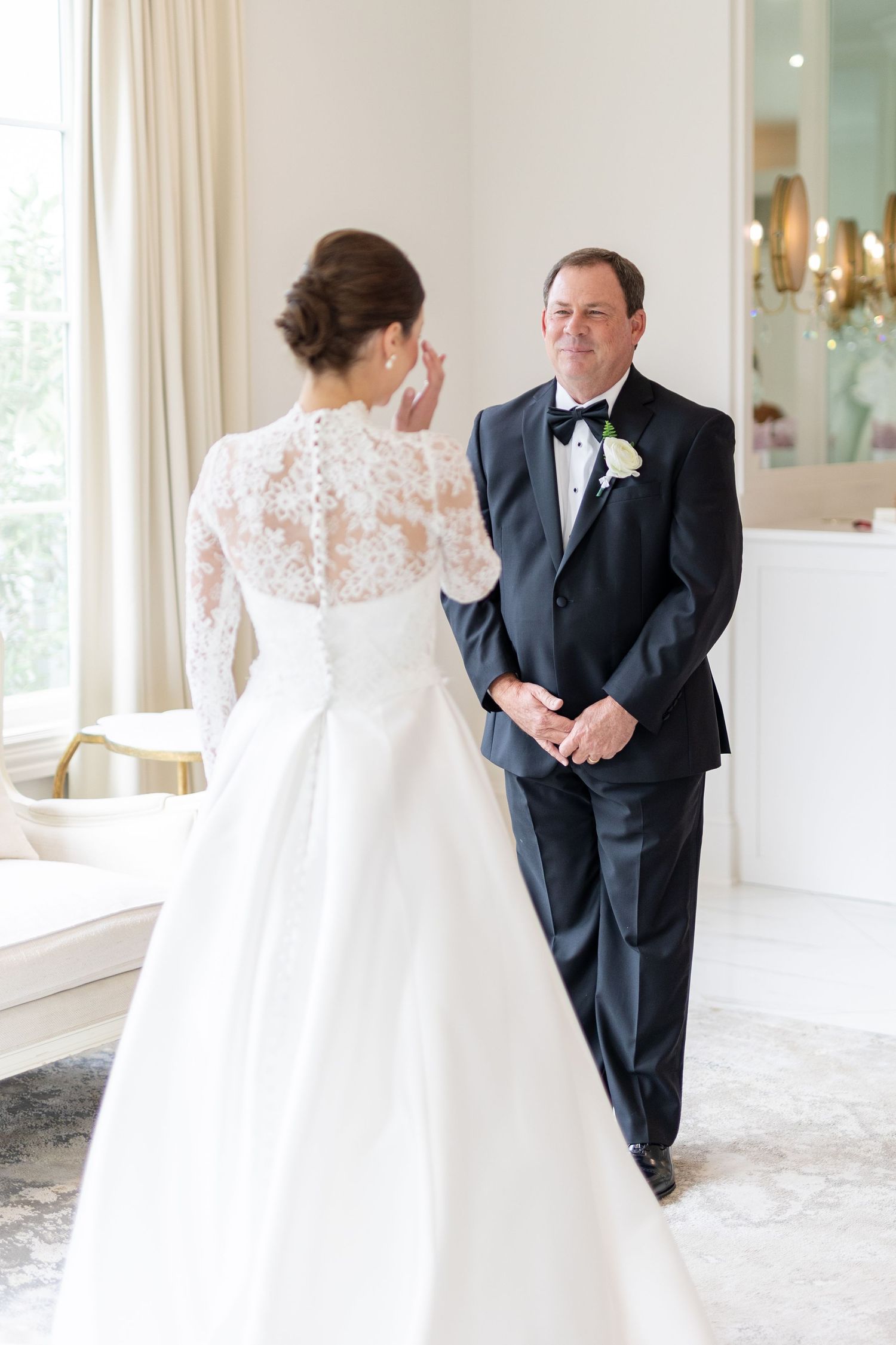 Father gazes proudly at bride in stunning white lace back wedding dress during first look.