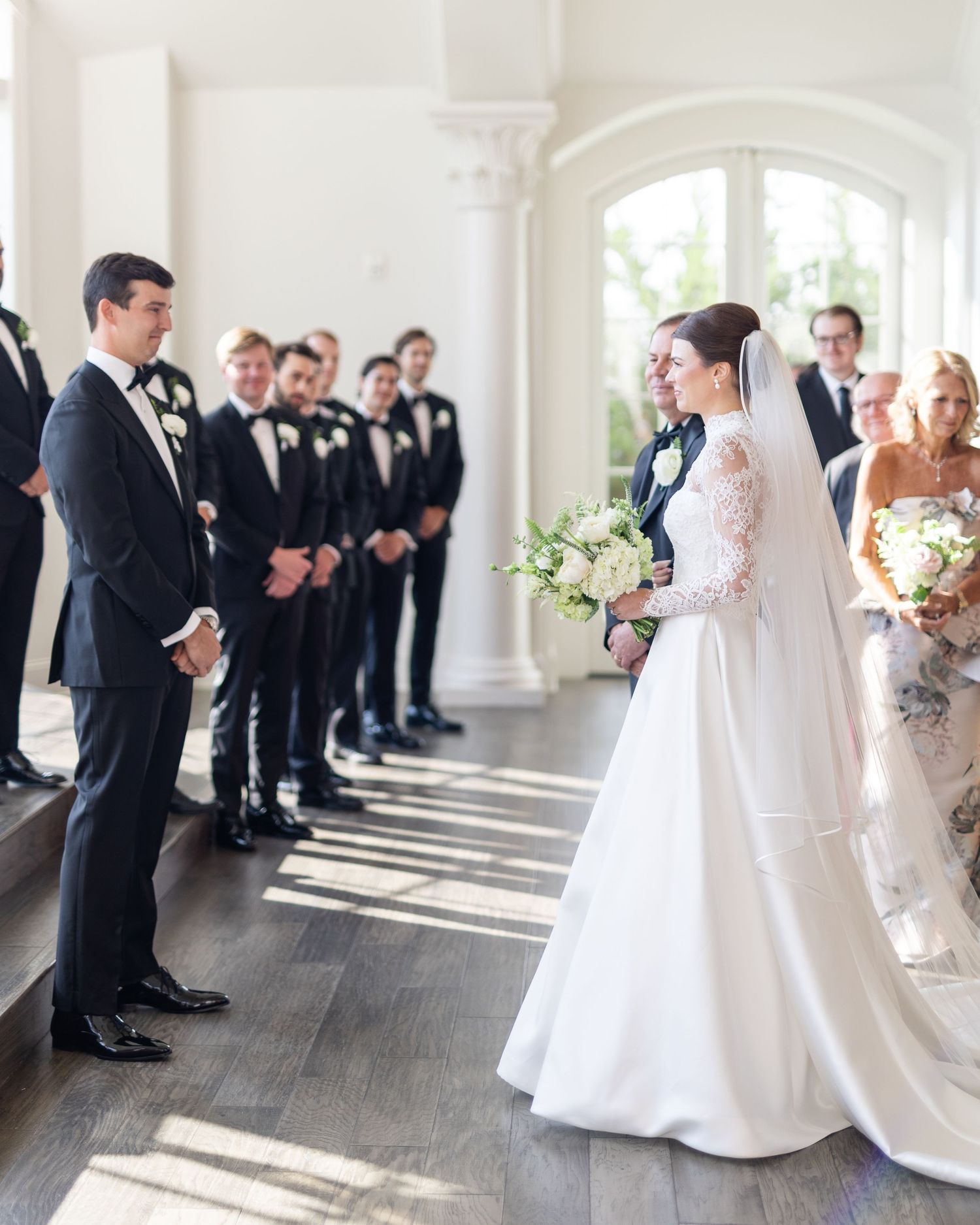 Bride and groom share a first look moment at the altar surrounded by groomsmen in black tuxedos.