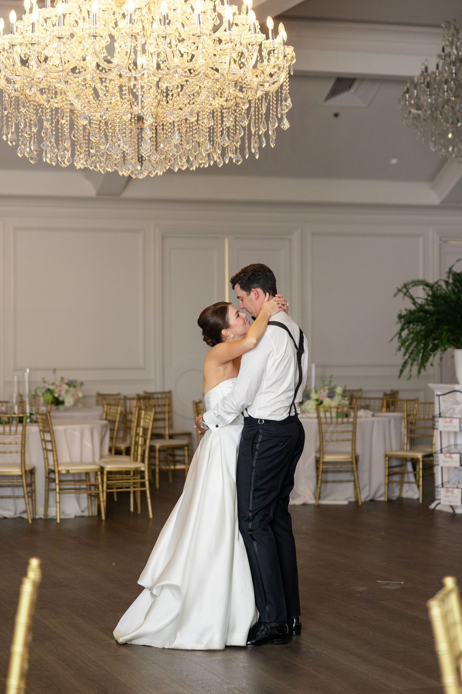 Bride and groom share first dance under grand crystal chandelier in elegant ballroom.