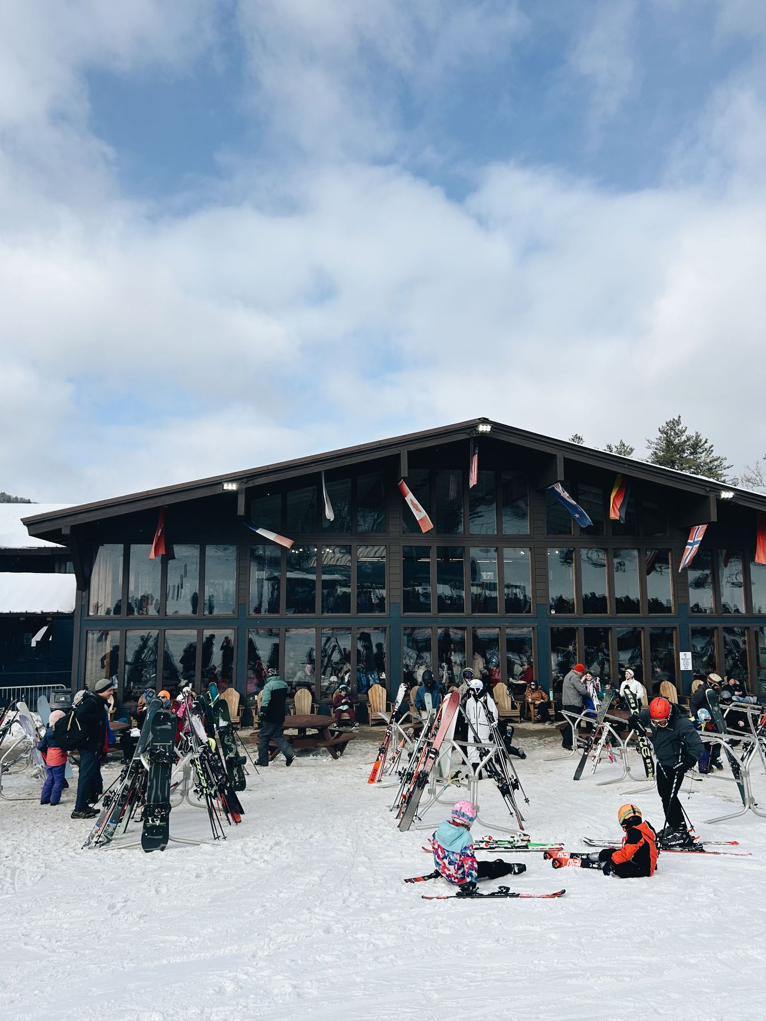 Skiers gather outside a large lodge at a snowy ski resort on a cloudy winter day.