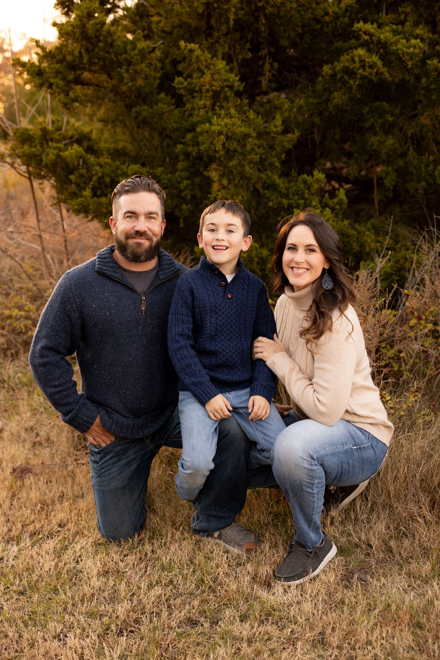Family in coordinating sweaters poses together on grassy hillside during golden hour sunset in autumn.