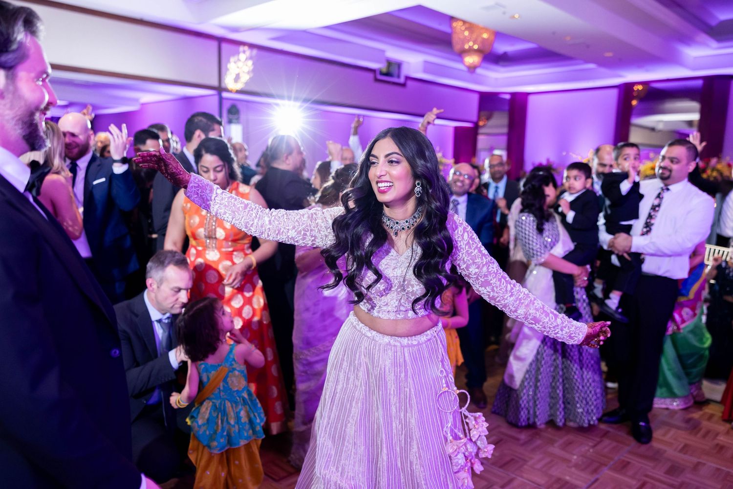 Guests dancing at a festive celebration in a ballroom with purple lighting and elegant decorations.