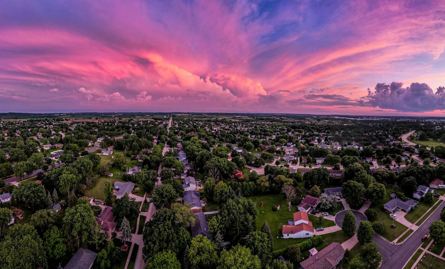 Aerial panoramic view of a suburban neighborhood under a stunning pink and purple sunset sky with dramatic clouds.