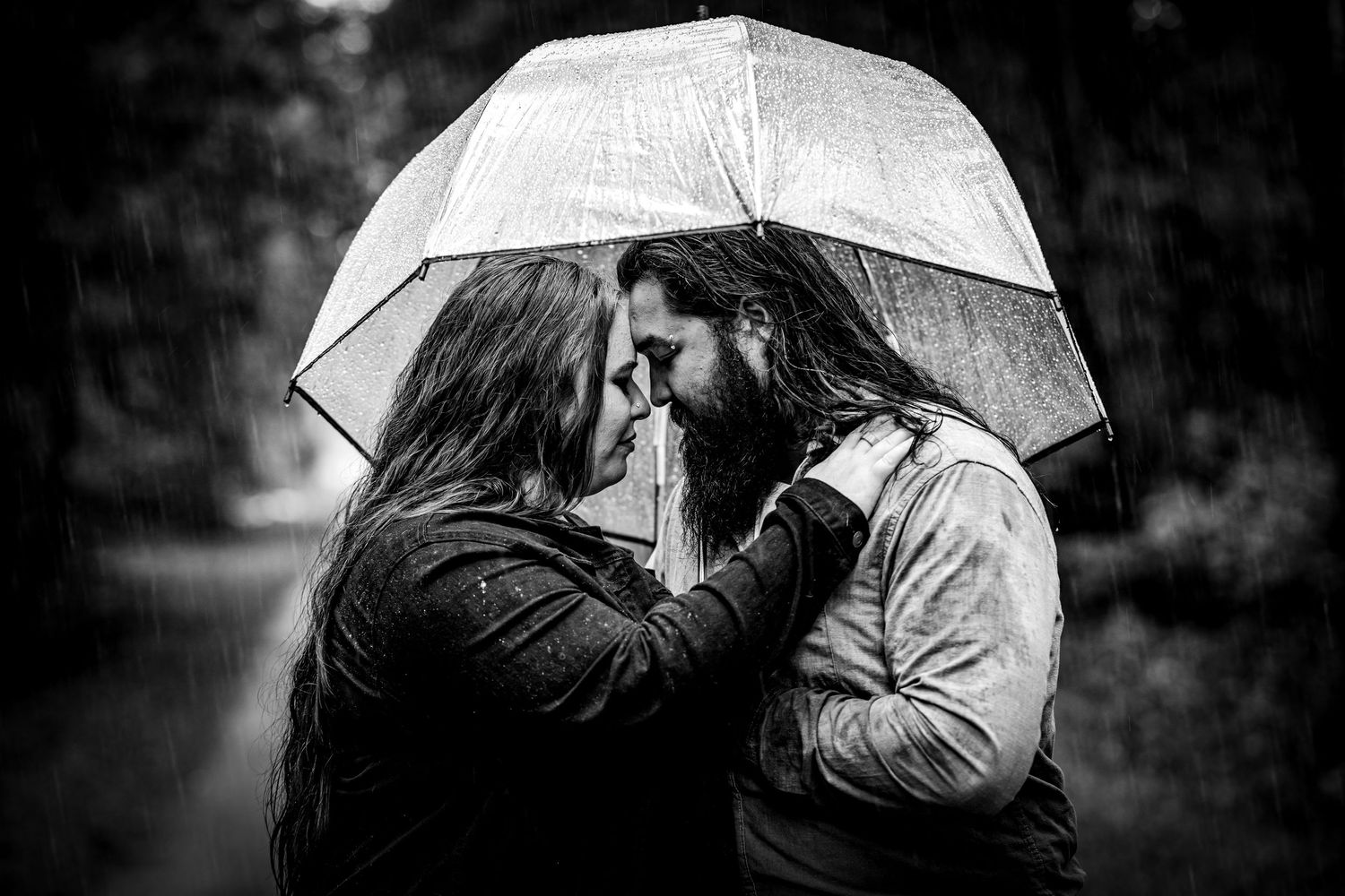 A romantic black and white photograph of a couple sharing an intimate moment under a white umbrella in the rain.