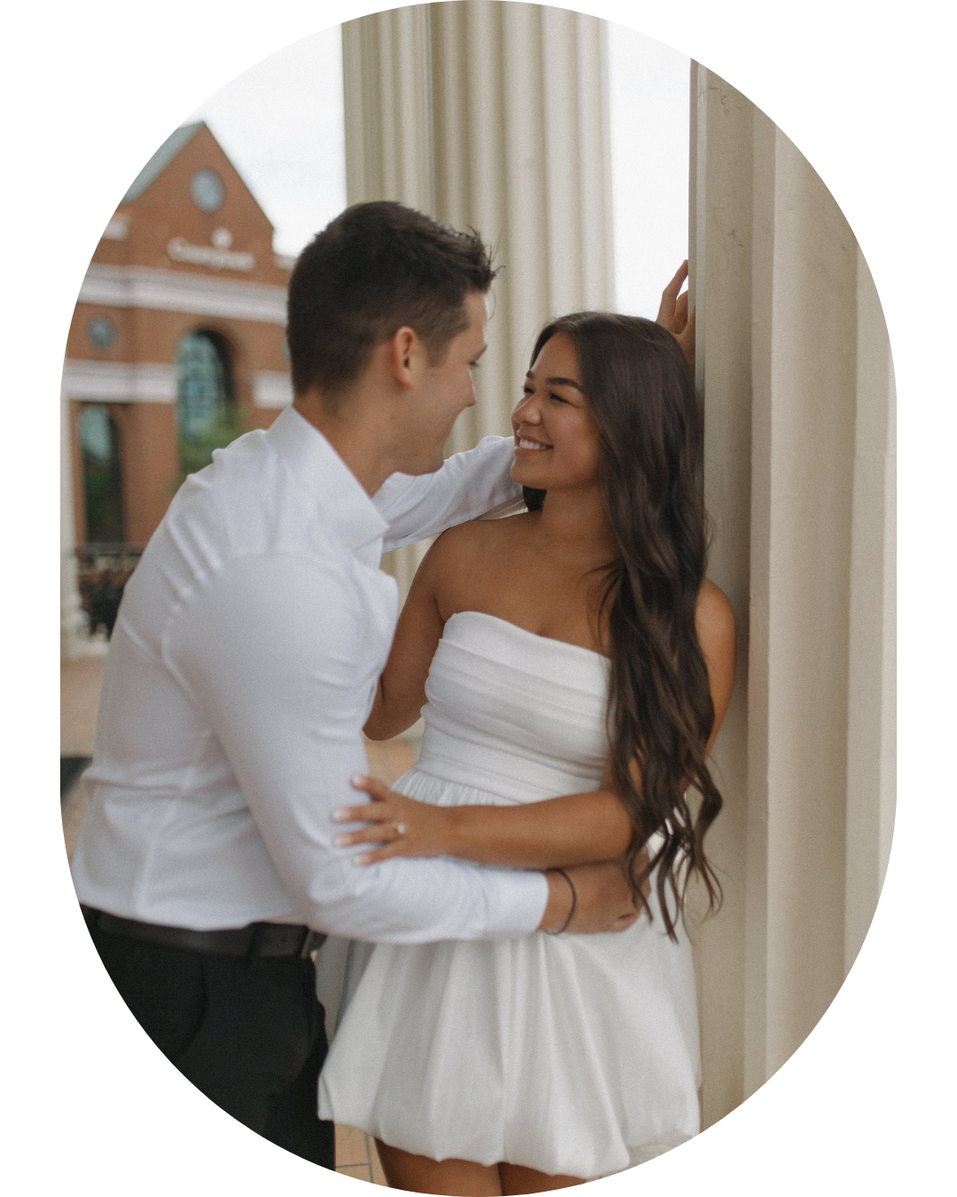 Happy couple sharing intimate moment in white wedding attire by window.