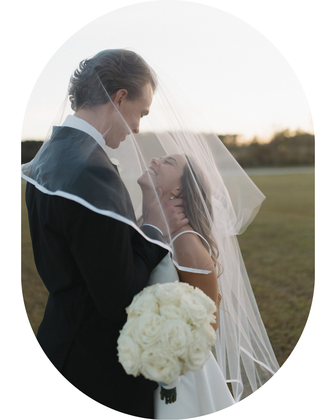 Romantic wedding portrait of couple embracing outdoors with white bouquet at sunset.